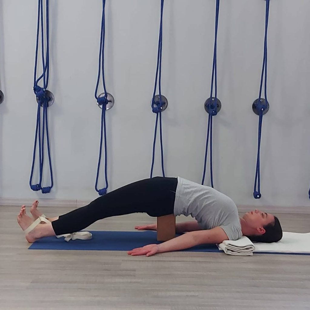 L'insegnante di Iyengar yoga Erika Beltrame esegue Setu Bandha Sarvangasana supportato con mattoncino e cinghia nella scuola Kalishiva Yoga a Torino