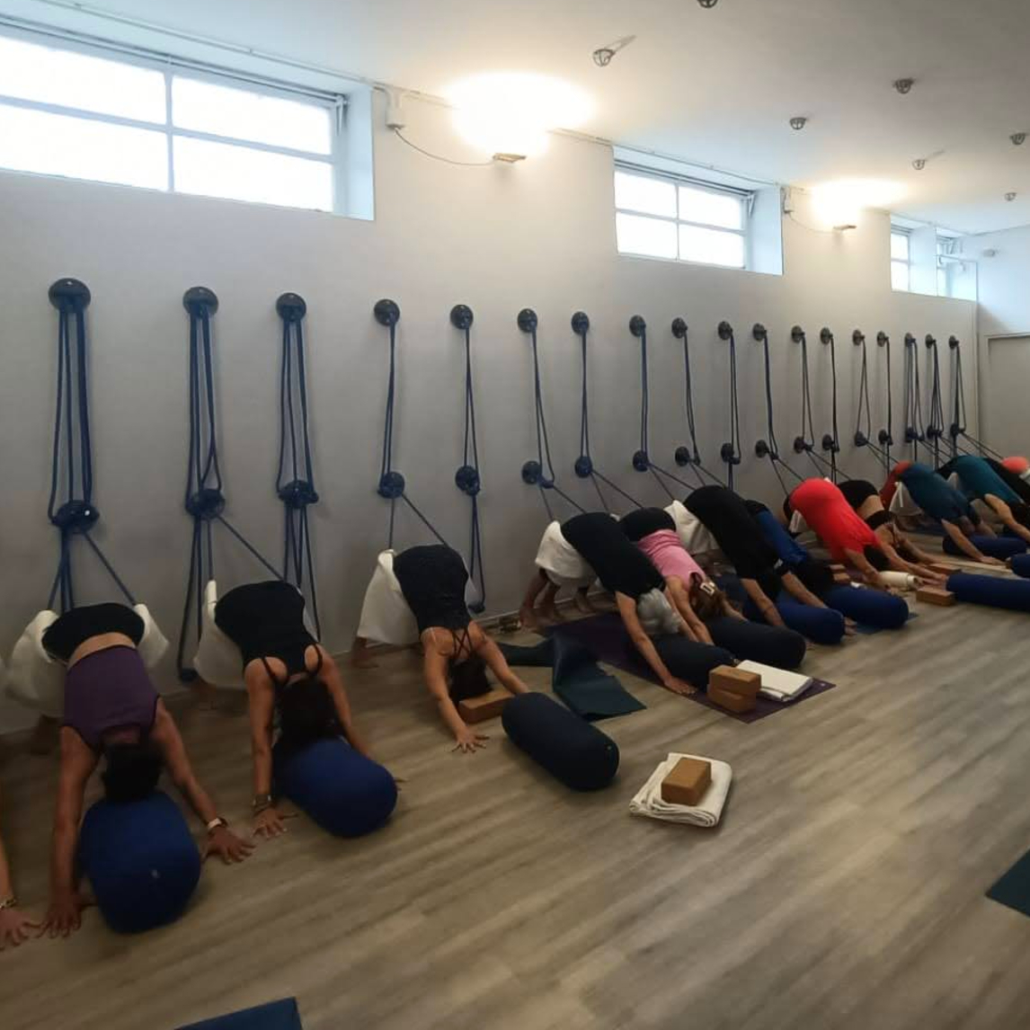 Allievi durante la posizione del cane a testa in giù Adho Mukha Svanasana con supporto di corde alla parete e bolster da Kalishiva Yoga Torino